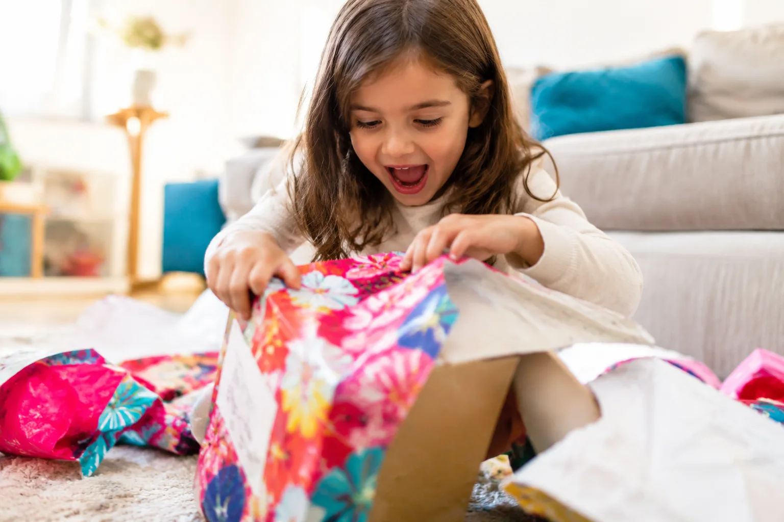 Young child excitedly opening a wrapped toy gift box, colorful wrapping paper scattered on the floor, bright cheerful indoor