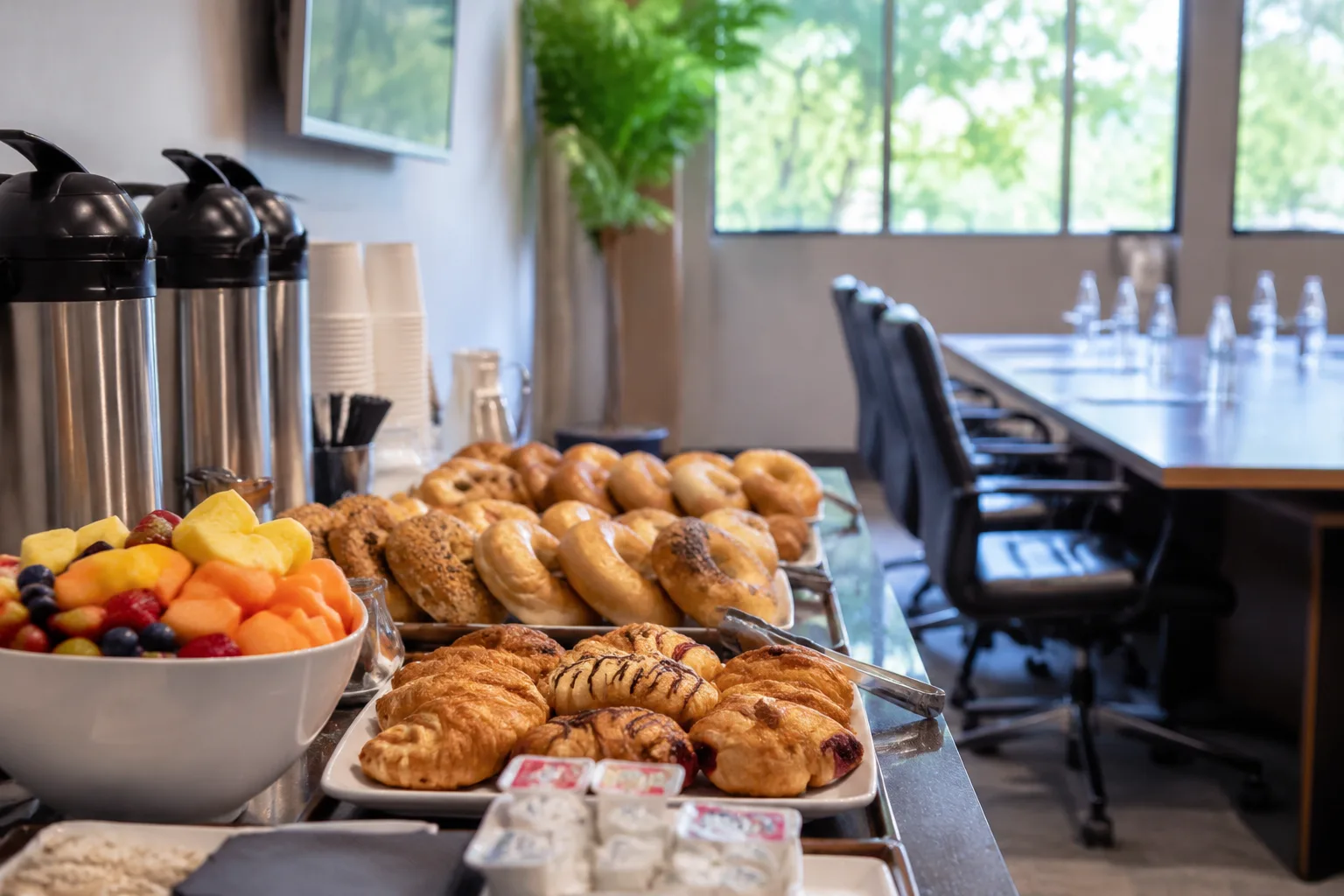 A photorealistic image of an office conference room breakfast catering setup with a continental spread of pastries, bagels, fresh fruit,