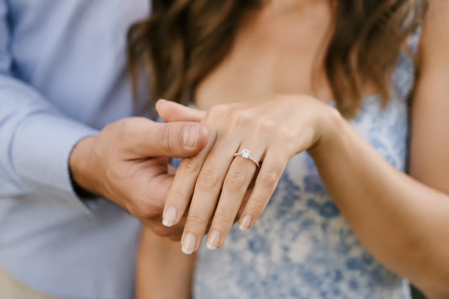 Couple's hands together showing off a new engagement ring, warm candid lighting, celebratory mood, shallow depth of field