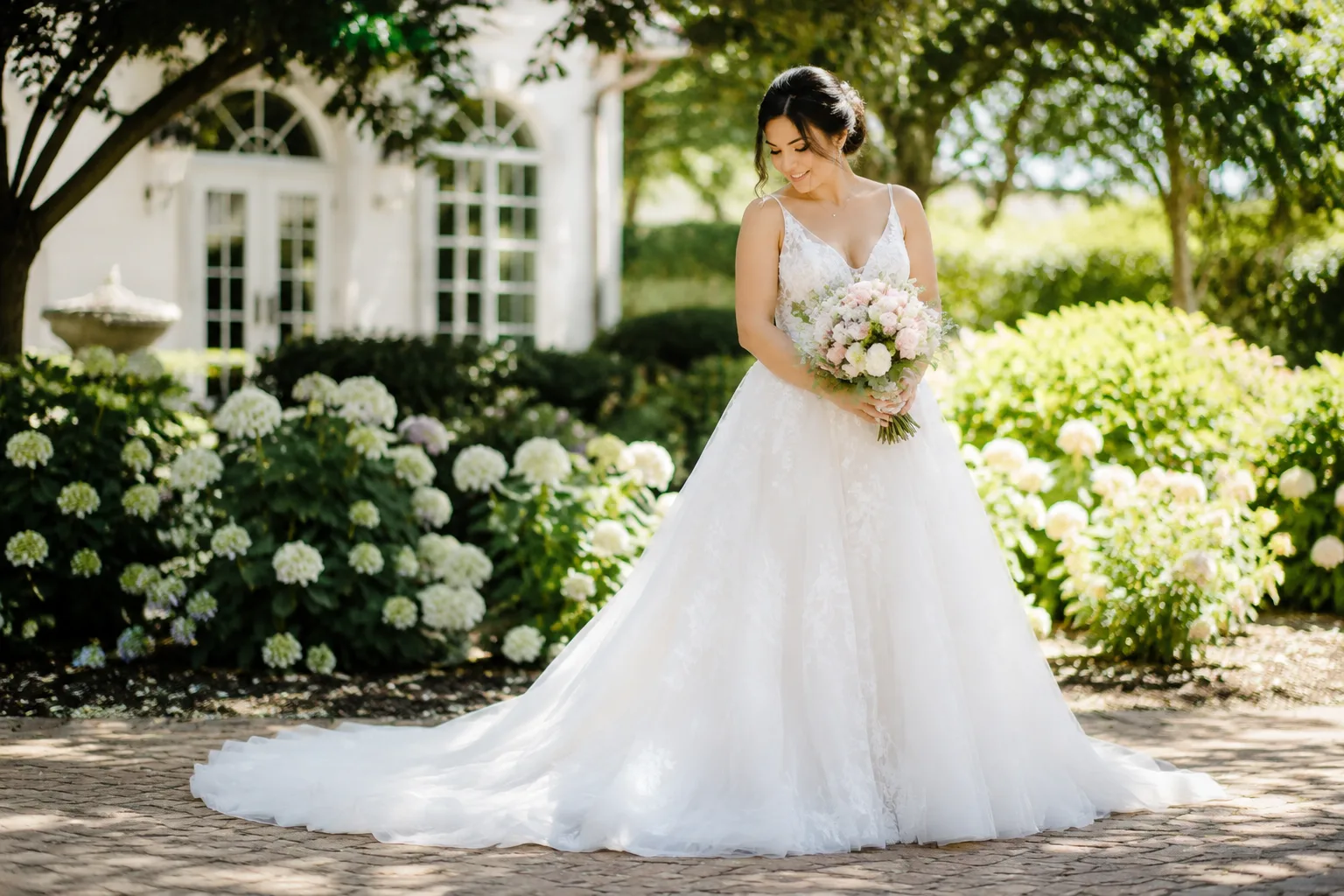 Bride in a flowing A-line wedding gown standing in a sunlit garden, full-length view
