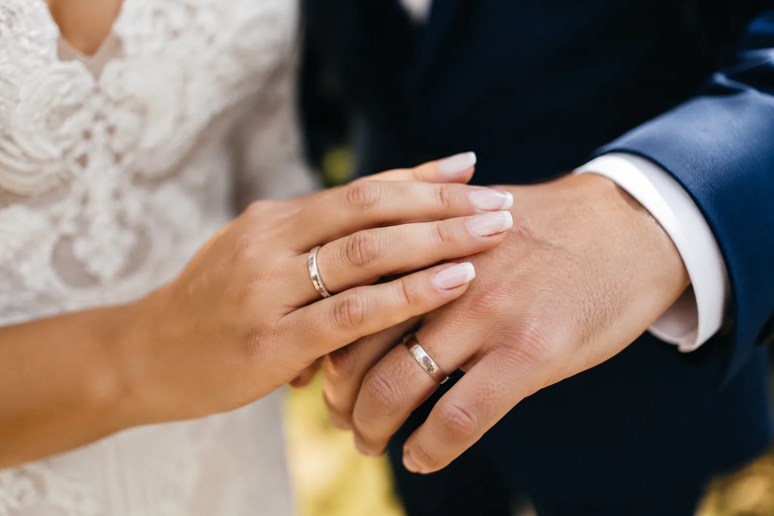 Couple's hands clasped together showing off their wedding bands, soft natural outdoor light, warm tones
