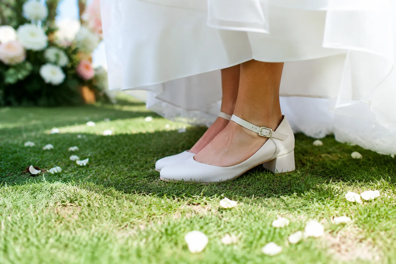 Bride's feet in comfortable low block-heel bridal shoes standing on grass at an outdoor garden wedding, sunny